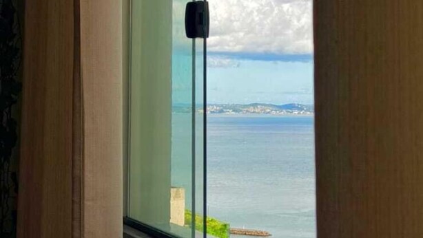 A room with a large window overlooking a body of water and a distant shoreline. - Stylish Loft in Salvador's Historic Center – Walk to Pelourinho (Salvador)