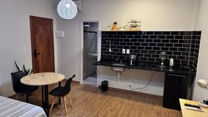 A compact kitchen with a black tiled backsplash, a small refrigerator, a sink, and a round dining table with chairs. - Stylish Loft in Salvador's Historic Center – Walk to Pelourinho (Salvador)