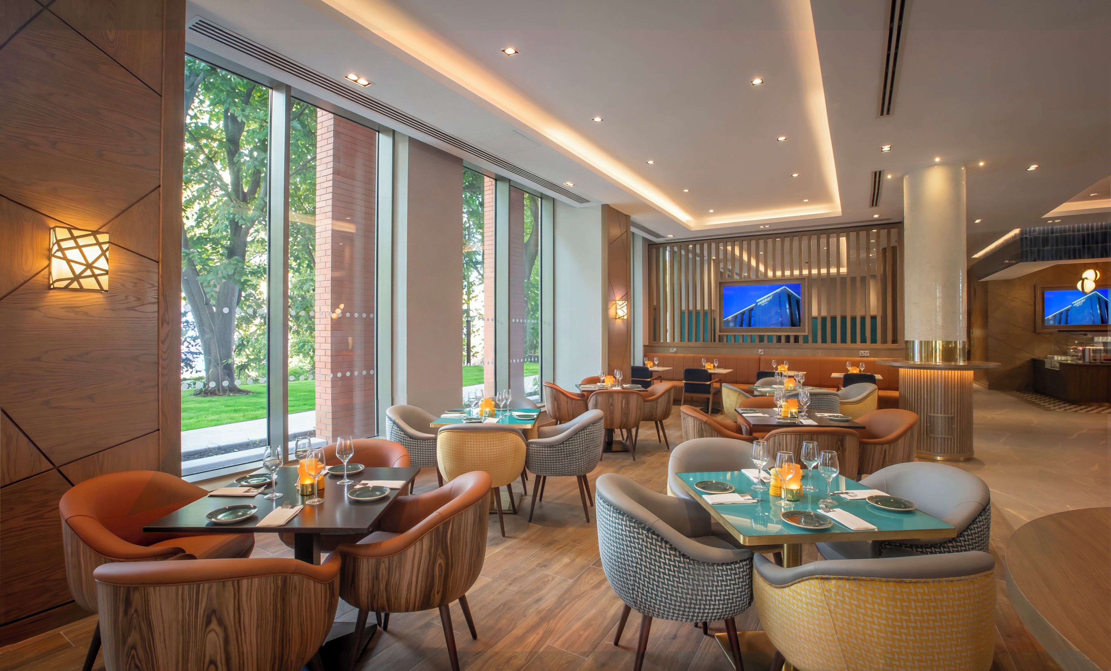 A modern restaurant with large windows, wooden flooring, and a TV screen displaying a building.