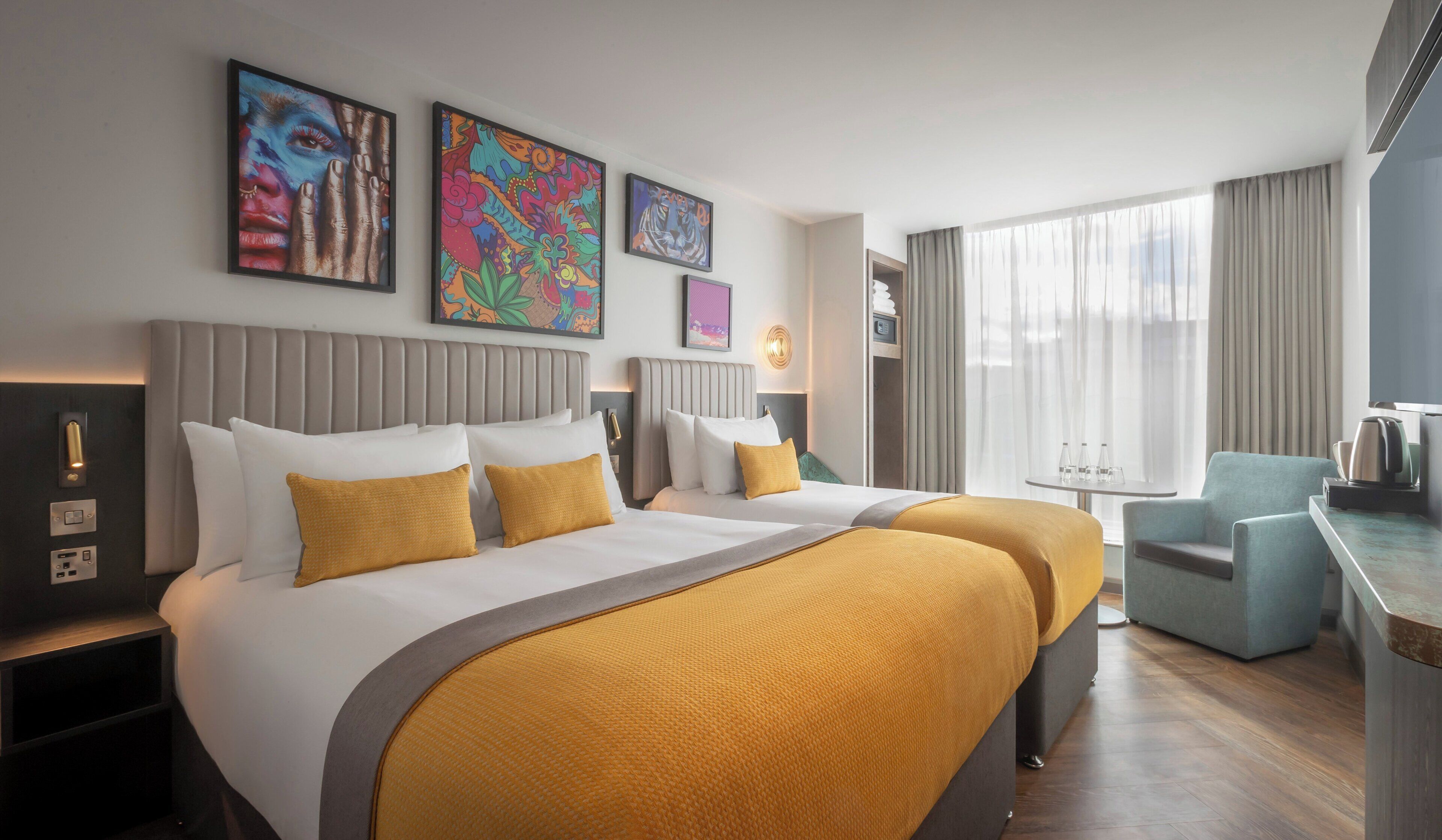 A hotel room with two beds, a desk, a chair, and artwork on the walls.