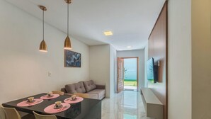 A modern dining area with a table set for four, a sofa, and a TV mounted on the wall. - Aprts in a Condomin. w/ Pool and Bbc, Imbassai - Foss (Mata de São João)