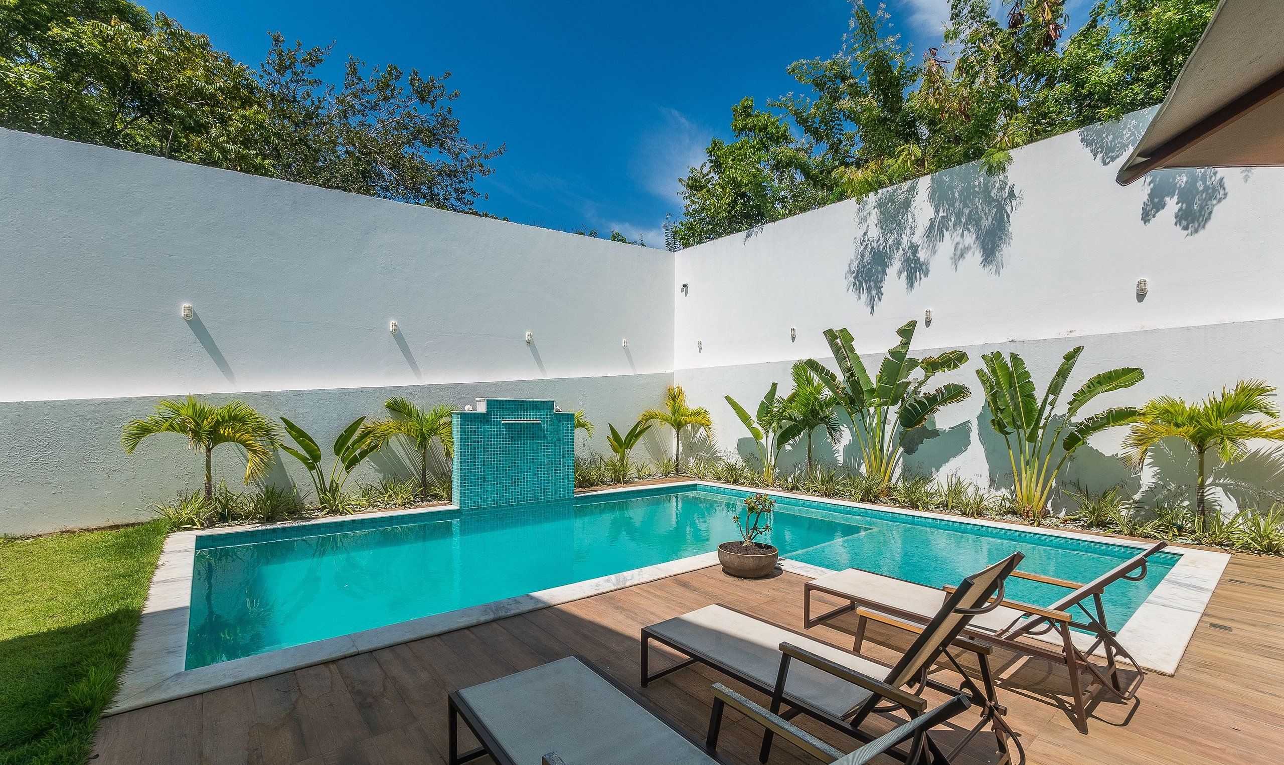 Une piscine rectangulaire dont le bord est recouvert de carrelage, entourée d’une terrasse en bois et de chaises longues.