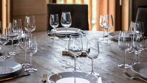 Una mesa de comedor dispuesta con copas de vino y platos, un candelabro y vistas a montañas desde una puerta abierta.