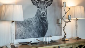 Una habitación con un cuadro grande de un ciervo en la pared, una consola de madera con objetos decorativos y dos lámparas a cada lado.