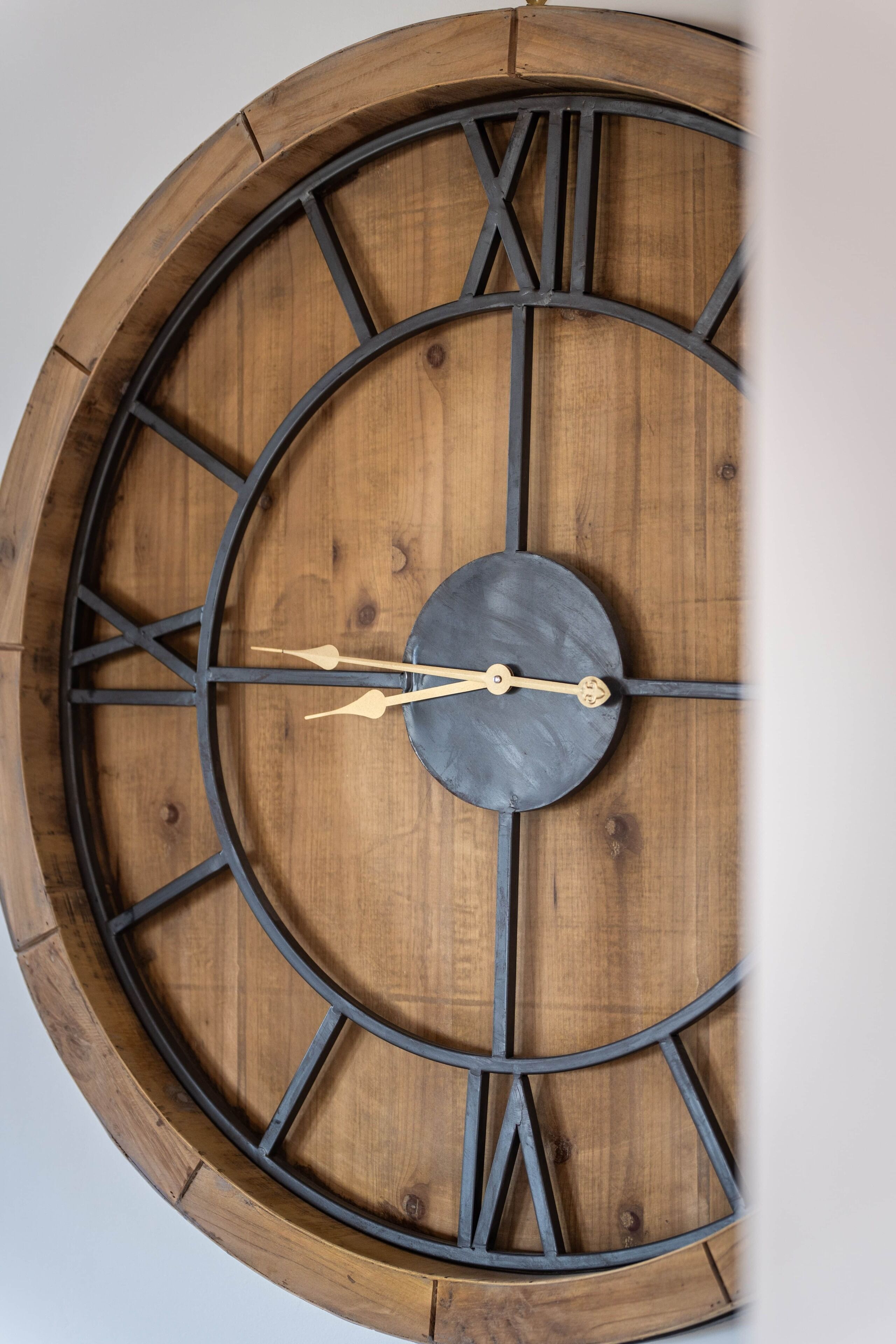 Een grote houten wandklok met Romeinse cijfers en een ronde wijzerplaat.