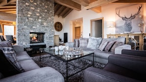 Una sala de estar acogedora con chimenea de piedra, asientos cómodos y una obra de arte con ciervos en la pared.