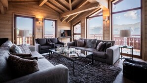 Un salón acogedor con chimenea, asientos cómodos y grandes ventanales con vistas a las montañas.