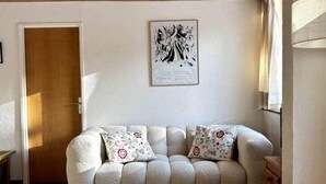 Ein gemütliches Wohnzimmer mit einem Holztisch, einer Couch mit gemusterten Kissen und einem gerahmten Kunstwerk an der Wand.
