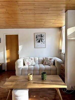 Uma sala de estar acolhedora com uma mesa de madeira, um sofá com almofadas estampadas e uma obra de arte emoldurada na parede.