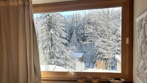 Ein Schlafzimmer mit Fensterblick auf einen verschneiten Wald, einem Heizkörper und einem Bett mit gemustertem Überwurf.