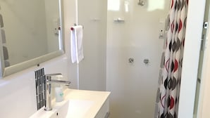 A bathroom with a white vanity, a mirror, a shower, and a patterned curtain.