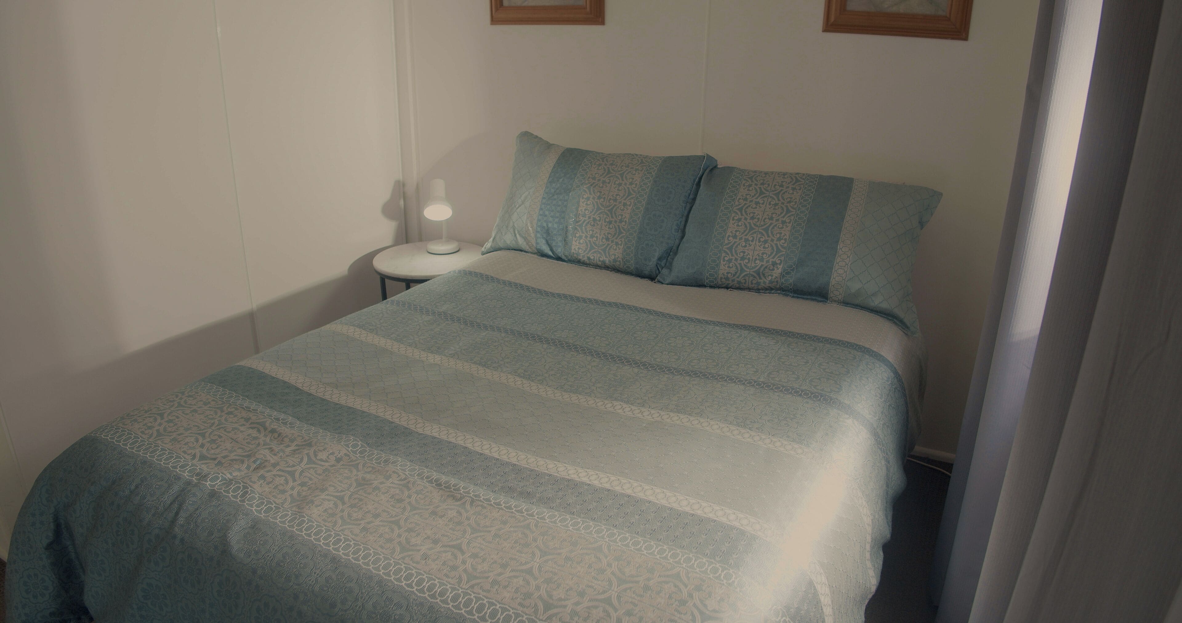 A neatly made bed with a patterned bedspread and two pillows, a bedside lamp, and a small table.
