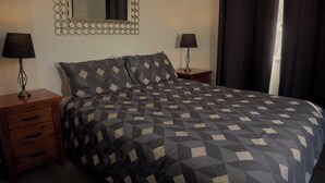 Un letto rifatto con cura, con copriletto a fantasia geometrica, due comodini con lampade e uno specchio appeso al muro.