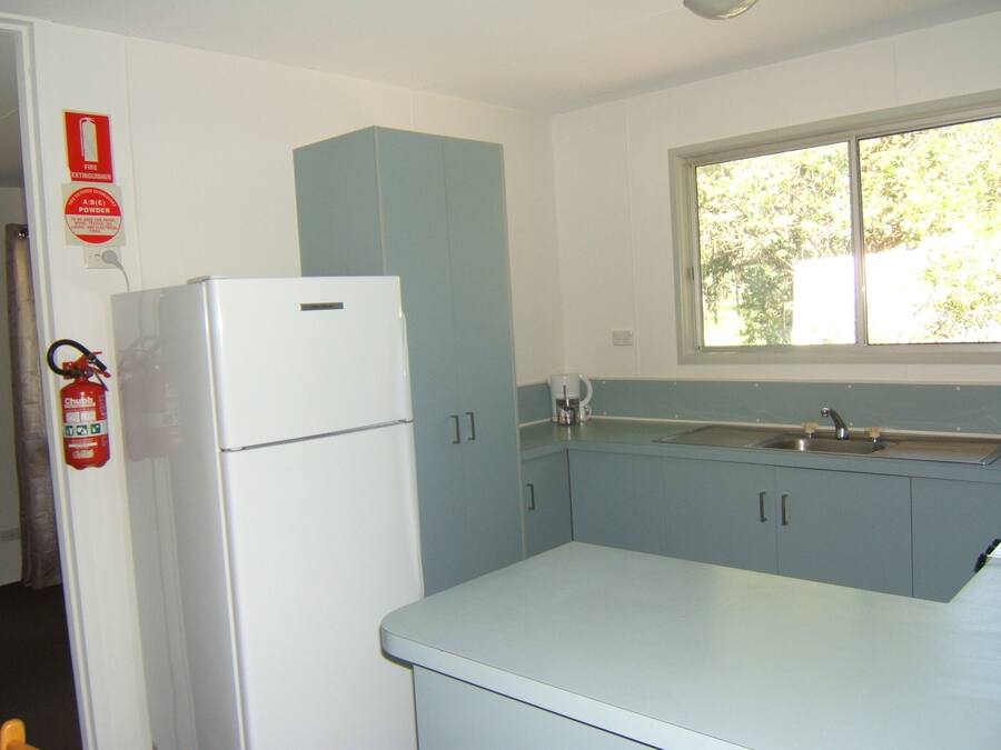 A compact kitchen with a white refrigerator, blue cabinets, a window with a view, and a fire extinguisher on the wall.