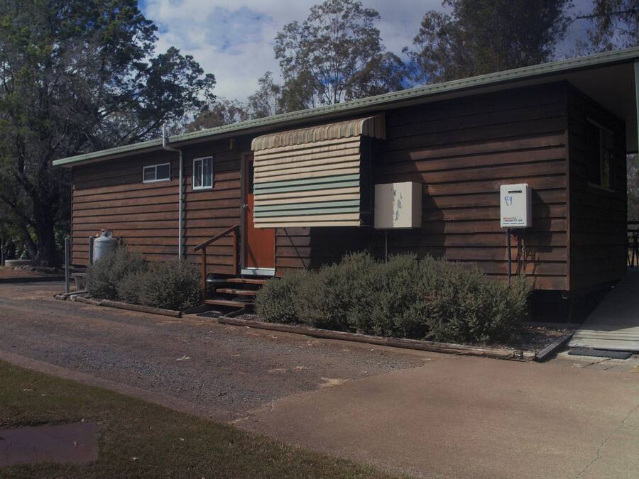 Un bâtiment en bois à deux étages, doté d’un porche couvert, d’une petite entrée à l’avant et d’un coffret de raccordement électrique visible.