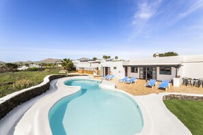 Un espace piscine au design incurvé, entouré d’un mur de pierre et jouxtant un bâtiment à la façade blanche surmontée d’une petite coupole.