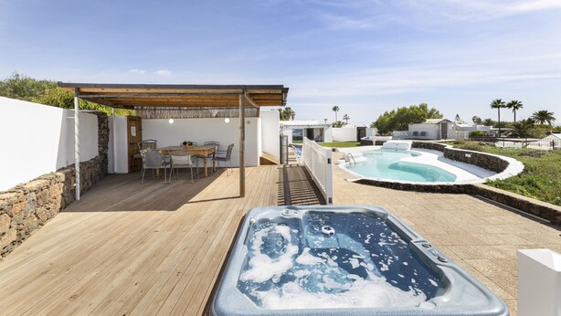 Una terrassa de fusta amb un banyera d'hidromassatge, una piscina i una zona d'estar coberta amb una taula i cadires.