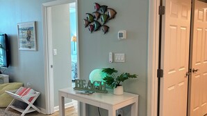 Une pièce avec une table blanche, une décoration représentant une planche de surf, une décoration murale en forme de poisson, une enseigne sur le thème de la plage et une porte donnant sur une autre pièce.