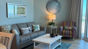Un salon avec un canapé gris, une table basse blanche, un fauteuil à rayures, un élément de décoration murale rond et un ventilateur de plafond.
