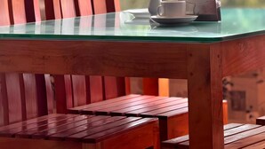 Una mesa de madera con cubierta de vidrio, una taza blanca y un florero blanco encima.