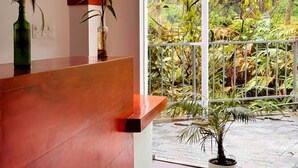 Zona de recepción con mostrador de madera, dos plantas en macetas y un amplio ventanal con vistas a un jardín exuberante.