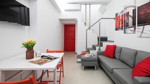 Un espacio habitable moderno con comedor, sofá, escalera y televisor de pantalla plana.