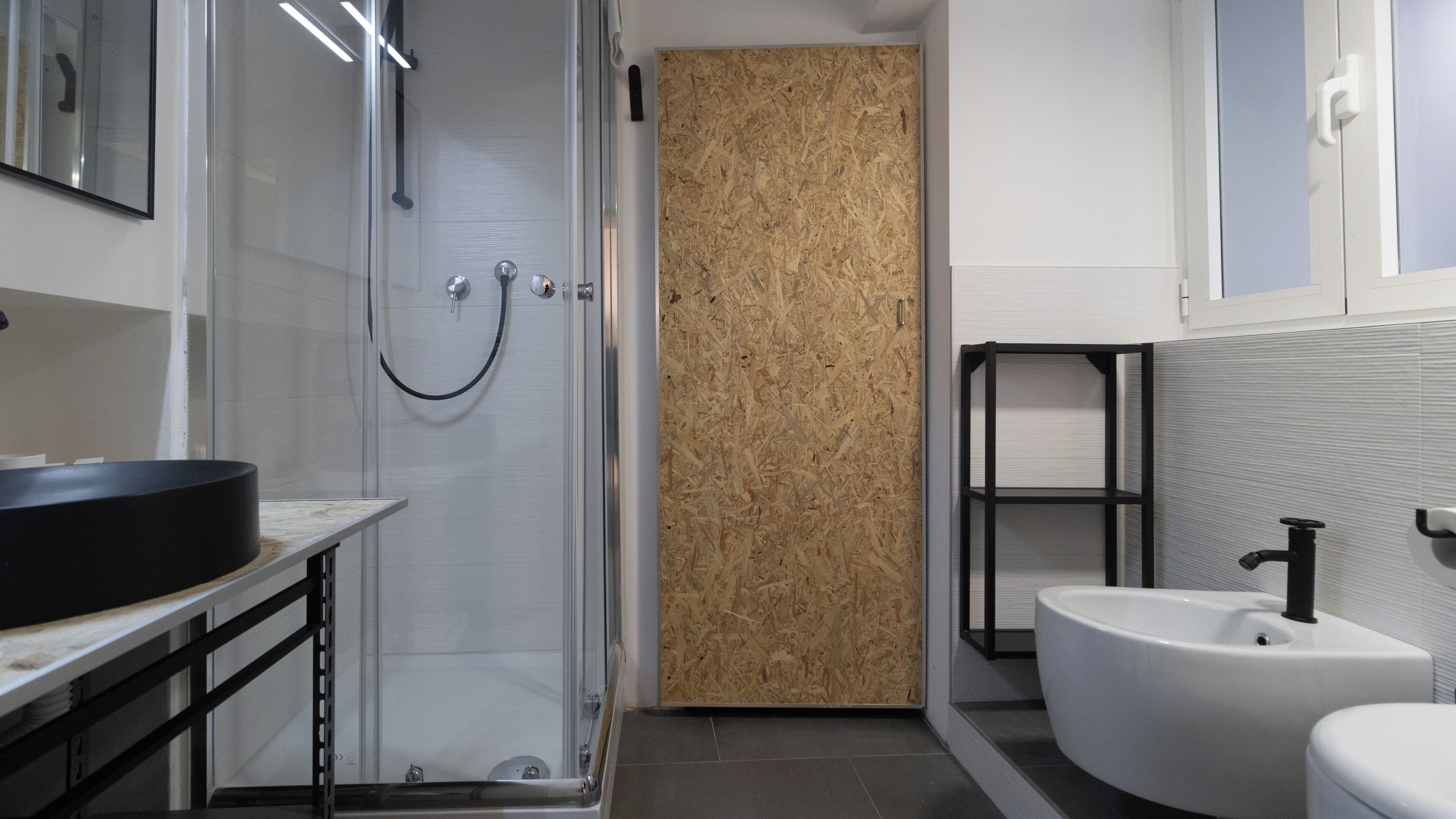 Een moderne badkamer met een glazen douchecabine, een zwarte wastafel en een wit toilet.