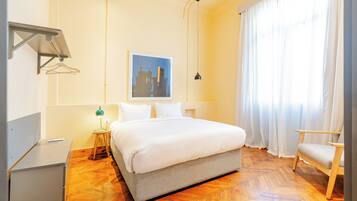 A hotel room with a bed, a desk, a chair, a lamp, and a painting on the wall.