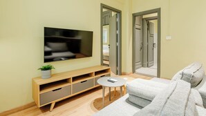 Un salon moderne doté d’un téléviseur à écran plat, d’une petite table ronde, d’un canapé gris et d’un meuble de rangement en bois.