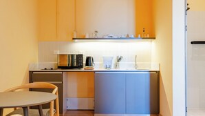 Une cuisine compacte équipée d’un four à micro-ondes, d’une machine à café et d’ustensiles de cuisine, le tout posé sur le plan de travail.
