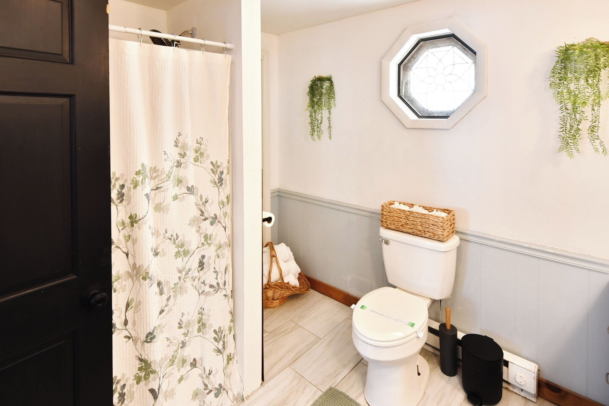 Un bagno con il water, una tenda da doccia, un cesto di asciugamani e una finestra con un motivo geometrico.