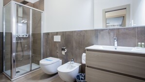 Un baño moderno con ducha envuelta en vidrio, un bidé y un lavamanos con tocador de madera.