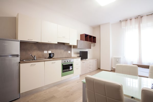A modern kitchen with a refrigerator, oven, and a dining area with a table and chairs. - Astoria Suite Apartments (Bologna)