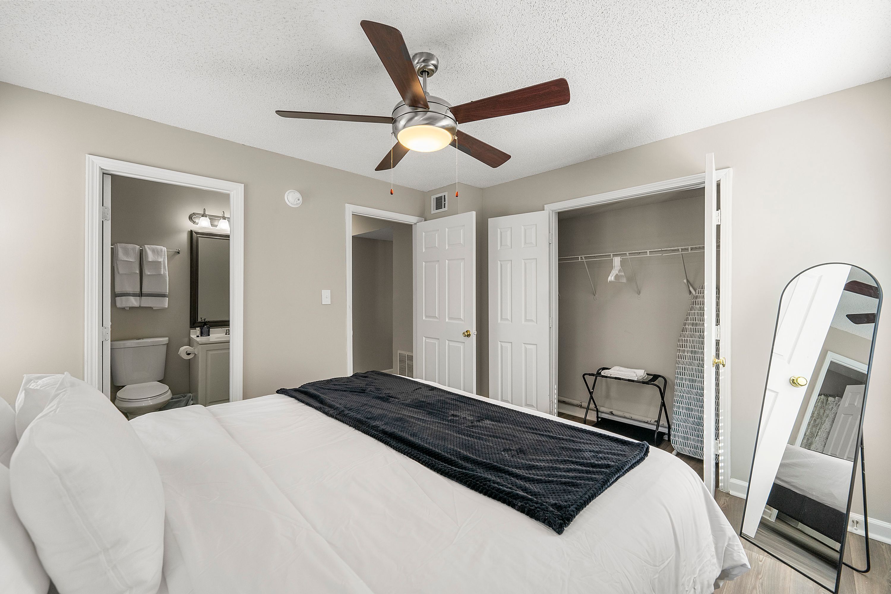 A bedroom with a bed, a ceiling fan, a walk-in closet, and a bathroom with a toilet and a mirror.