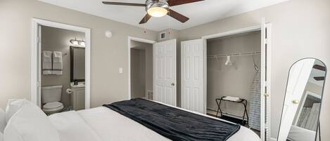A bedroom with a bed, a ceiling fan, a walk-in closet, and a bathroom with a toilet and a mirror.