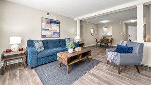 Een woonkamer met een blauwe bank, een houten salontafel en een grijze fauteuil.