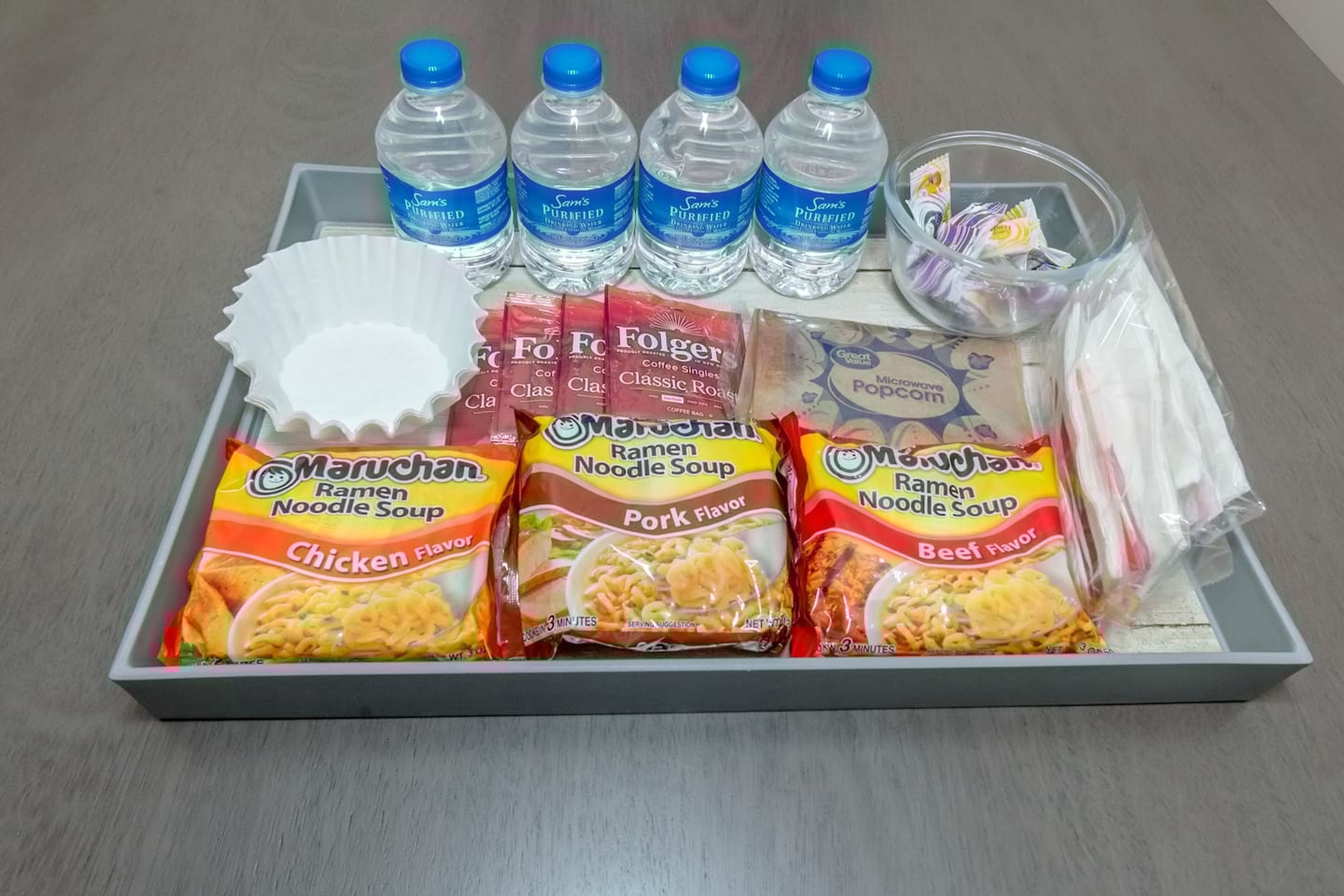 A tray with various food items including ramen noodles, coffee, and bottled water.