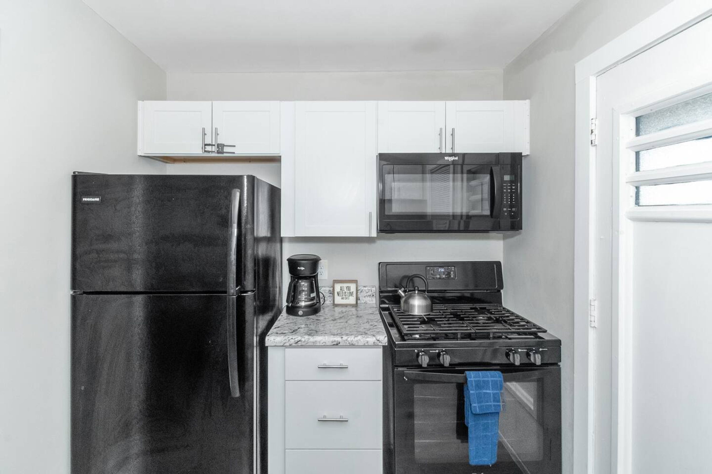 A compact kitchen with a stainless steel refrigerator, a microwave, a gas stove, and white cabinets.
