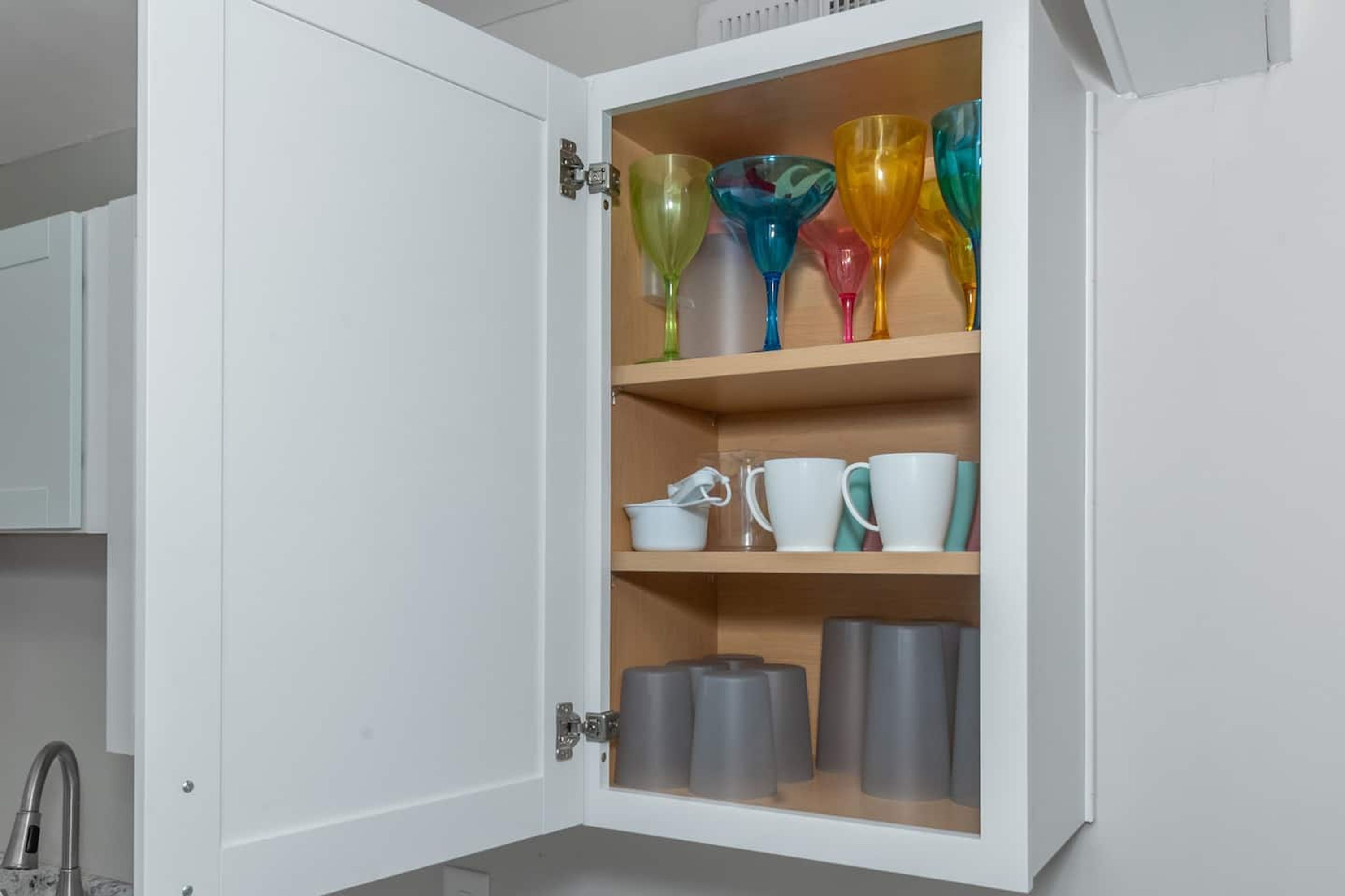 A cabinet with colorful glassware and mugs.
