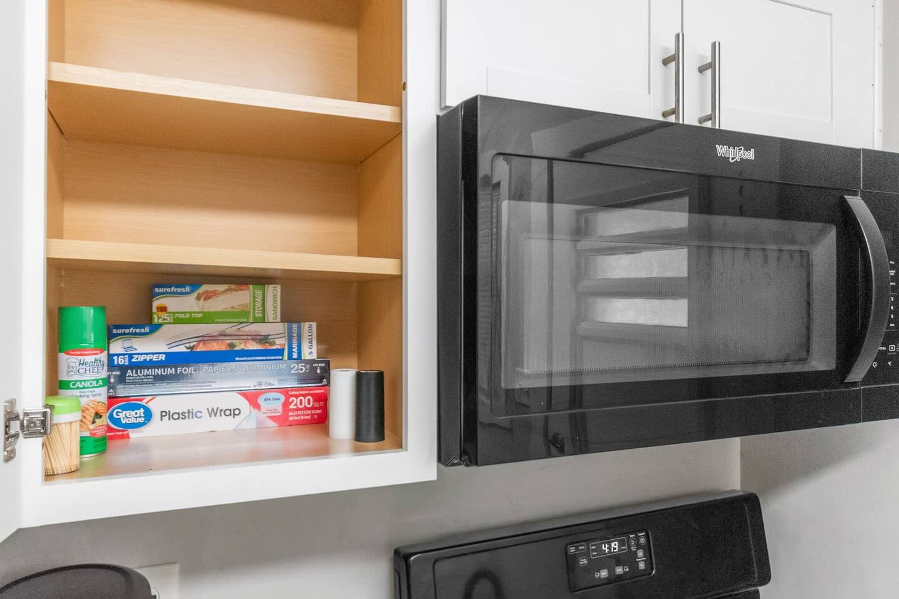 Een keuken met een zwarte magnetron en een witte kast eronder met verschillende keukenbenodigdheden.