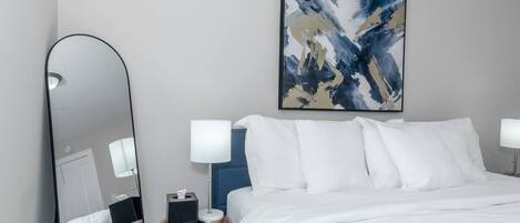 A hotel room with a large bed, two bedside lamps, a bedside table with a lamp, a mirror, and a painting on the wall.