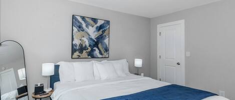 A hotel room with a large bed, a bedside table with a lamp, a mirror, and a door.