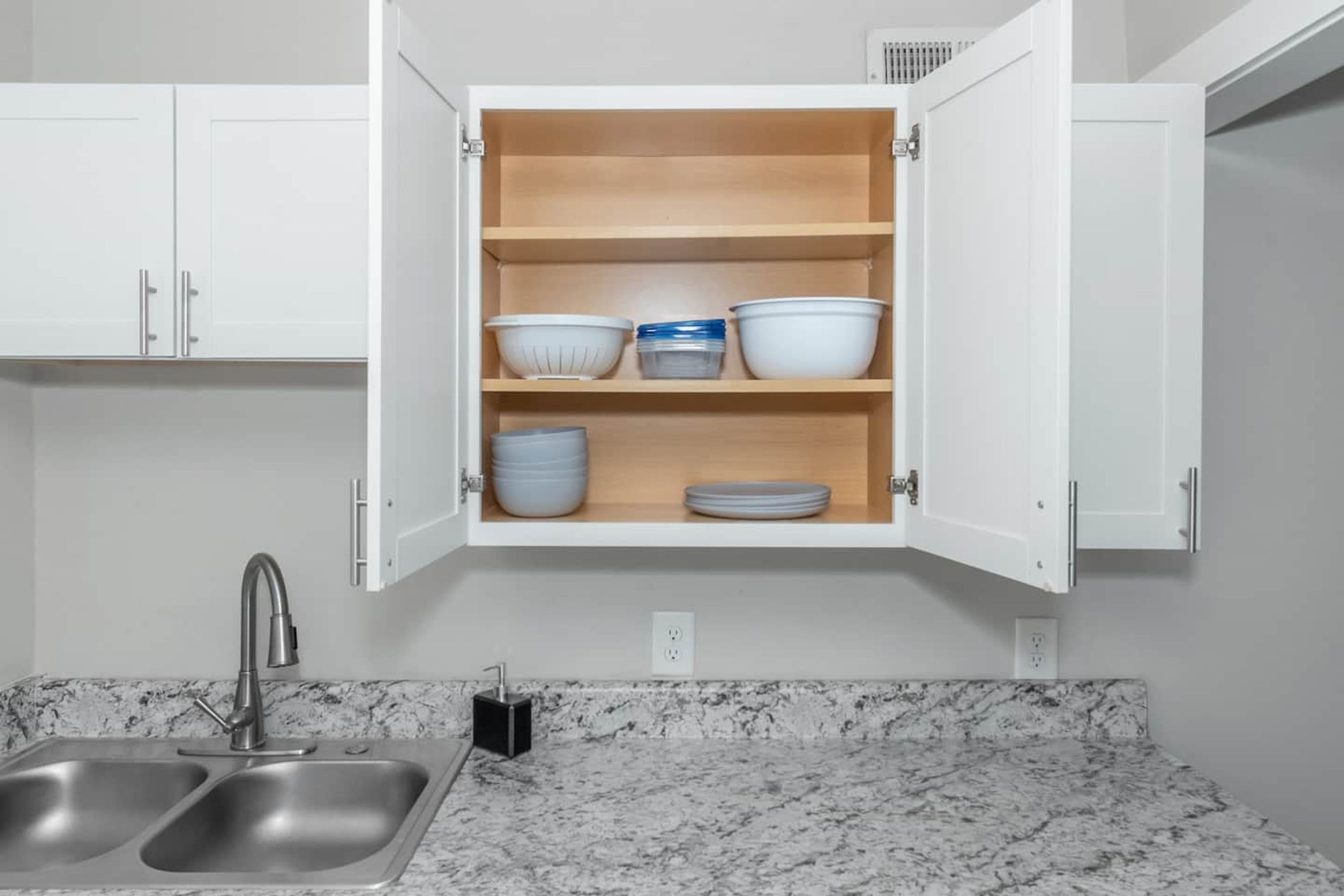 Een keuken met een dubbele spoelbak, witte kastjes en een marmeren aanrecht.