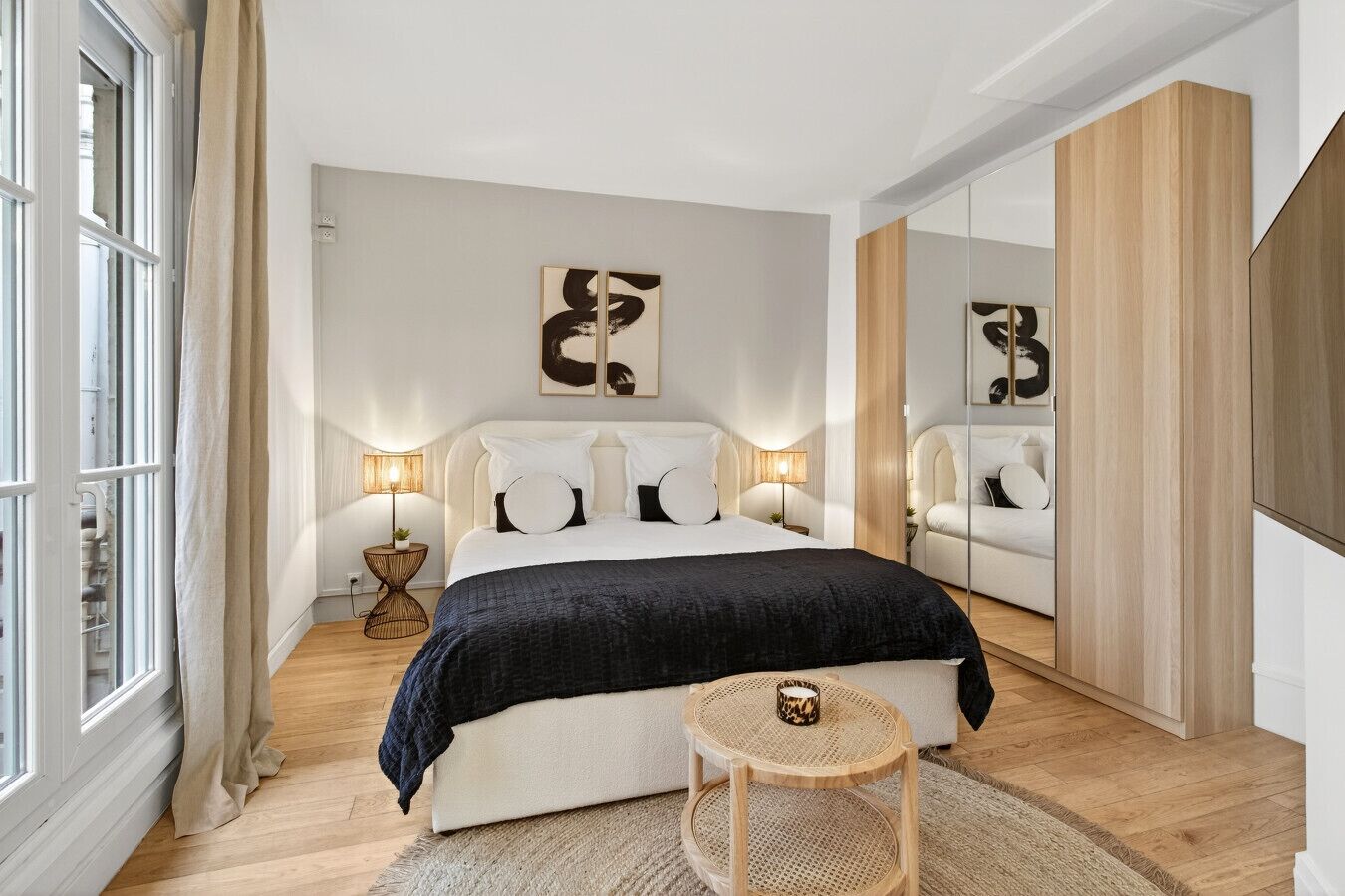 A modern bedroom with a large bed, bedside lamps, a small round table, and a mirror.