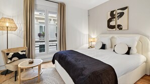 Quarto de hotel com uma cama grande, uma mesinha redonda, uma cadeira e vista para a varanda.