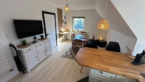 A modern kitchen with a wooden dining table, white cabinets, and a built-in TV. - House Königsee *Sternenblick* (Bad Oldesloe)