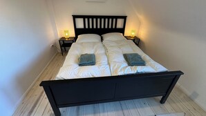 A bedroom with a black bed frame, white bedding, two bedside lamps, and a small plant on the wall. - House Königsee *Sternenblick* (Bad Oldesloe)