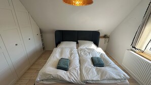 A bedroom with a bed, a hanging light fixture, a window with curtains, and a radiator. - House Königsee *Sternenblick* (Bad Oldesloe)