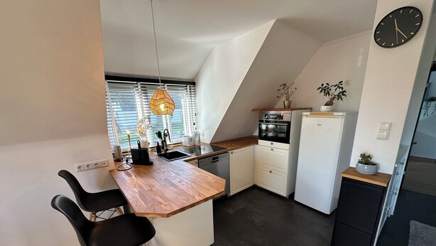 A compact kitchen with a wooden countertop, black chairs, a built-in oven, and a refrigerator. - House Königsee *Sternenblick* (Bad Oldesloe)