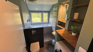 A compact bathroom with a toilet, washing machine, and a window providing natural light. - House Königsee *Sternenblick* (Bad Oldesloe)